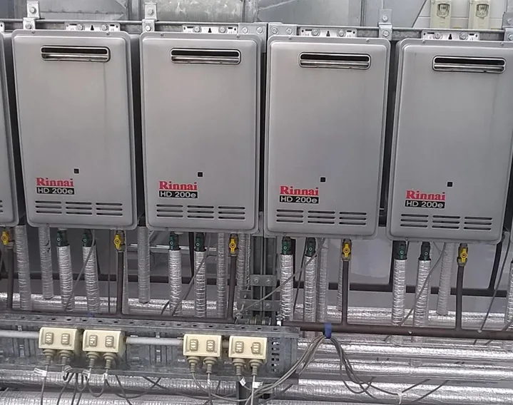 Four Rinnai HD200e commercial heaters with gas and water connections and isolation valves underneath