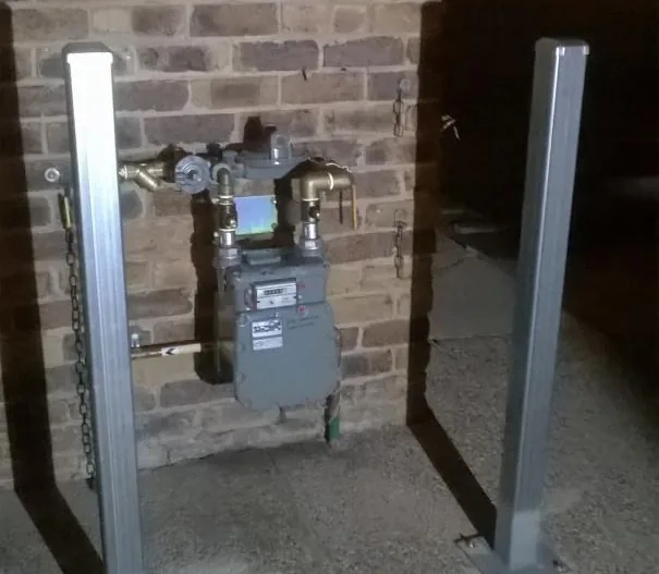 Gas meter and regulator protected by two steel bollards beside a brick wall