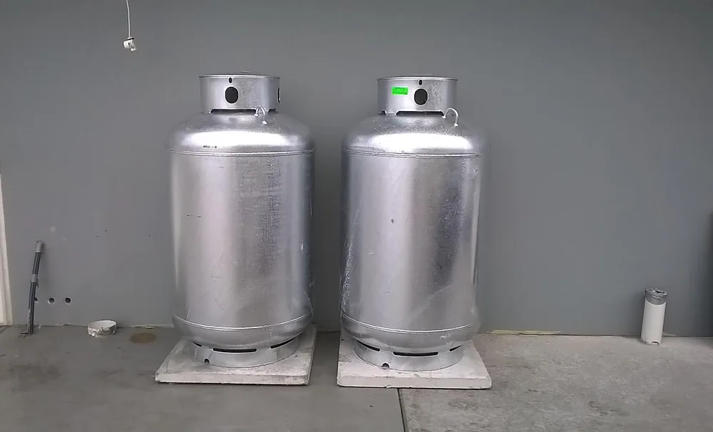 Two new LPG gas cylinders installed on pavers against a grey wall