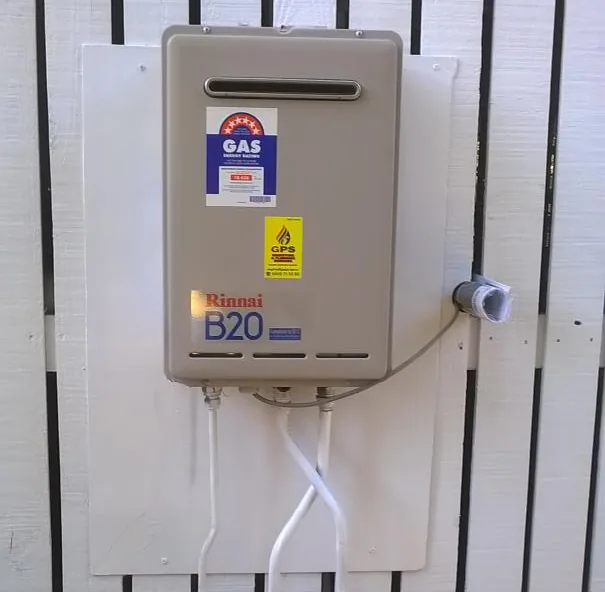 Rinnai B20 continuous-flow gas hot water unit with a GAS approval label and a GPS Gasfitting compliance sticker, mounted on a white fence